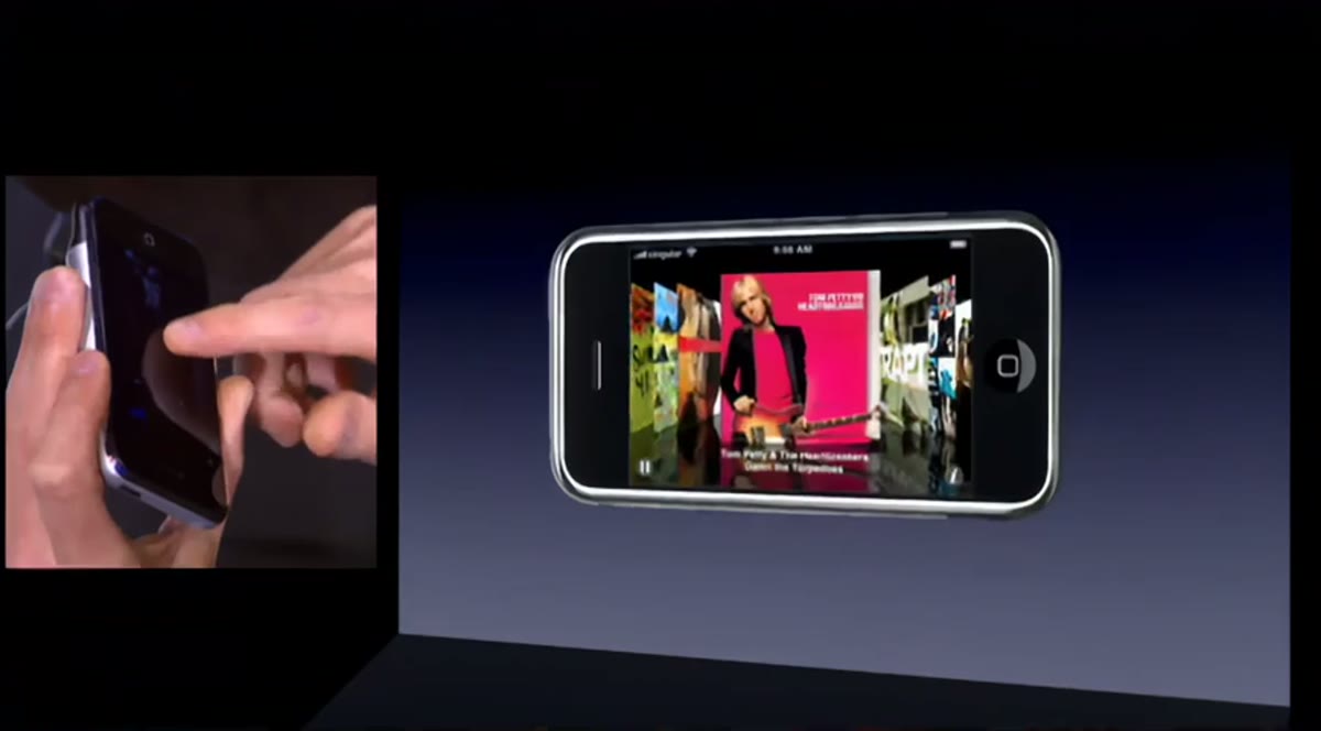 A close-up of a hand holding the first iPhone, its touchscreen visible.