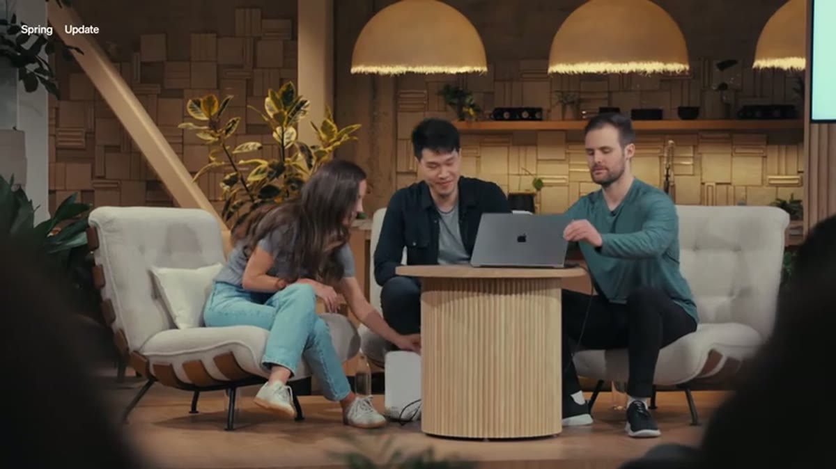 Three presenters gathered around a laptop on a lectern during a demo segment.